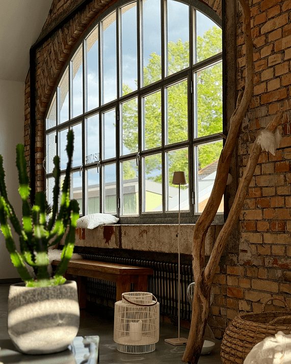 Eine Steinwand mit einem Gitterfenster und weiterer Deko auf einem Tisch davor.