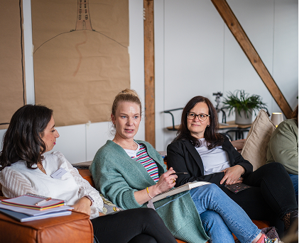 Drei Frauen sitzen auf einem Sofa und reden miteinander.