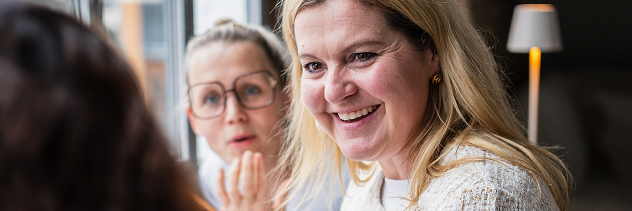 Zwei Frauen schauen nach vorne. Die Frau links sieht überrascht aus, die Frau rechts lächelt.
