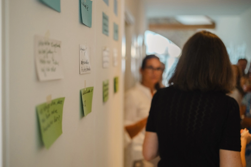 Post-its an einer Wand mit Menschen daneben